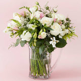 Bouquet of stunning fresh flowers in a clear vase on a pink background.
