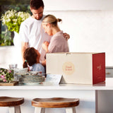 Family embracing in the background with a “Food is love” delivery box on the kitchen counter.